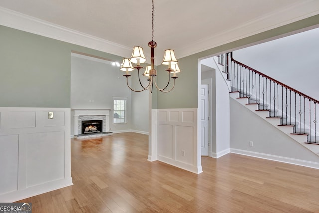 unfurnished dining area with ornamental molding, a stone fireplace, a chandelier, and light wood-type flooring