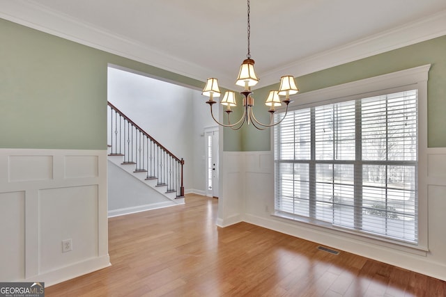 unfurnished dining area featuring crown molding, an inviting chandelier, and hardwood / wood-style flooring