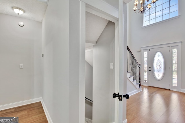 foyer entrance with hardwood / wood-style flooring, a towering ceiling, a wealth of natural light, and a notable chandelier