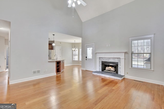 unfurnished living room featuring ceiling fan with notable chandelier, high vaulted ceiling, a fireplace, sink, and light hardwood / wood-style flooring