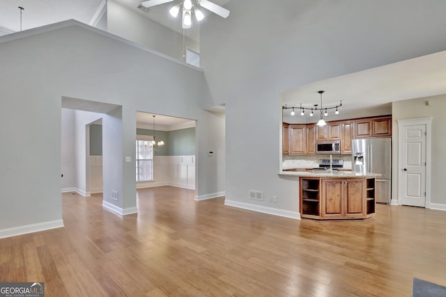 kitchen featuring pendant lighting, stainless steel appliances, tasteful backsplash, ceiling fan with notable chandelier, and light wood-type flooring