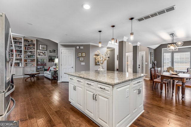 kitchen featuring stainless steel fridge, white cabinets, hanging light fixtures, a center island, and light stone counters