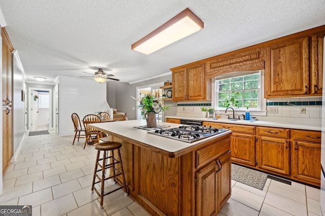 kitchen featuring sink, a kitchen island, stainless steel gas cooktop, a kitchen bar, and decorative backsplash