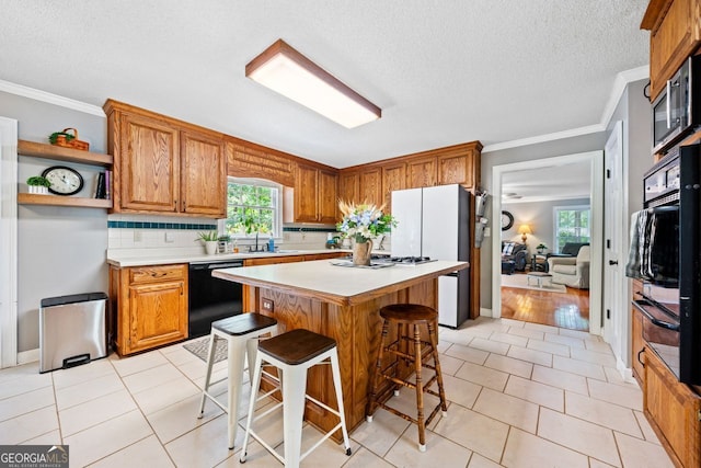 kitchen featuring light tile patterned flooring, sink, a center island, a kitchen breakfast bar, and black appliances