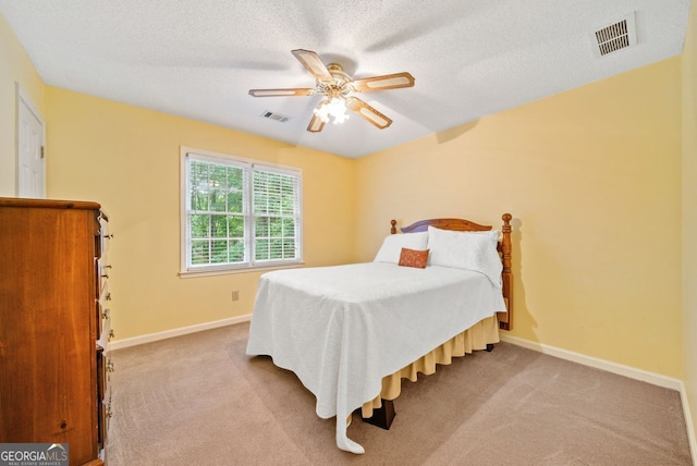 bedroom with ceiling fan, light carpet, and a textured ceiling