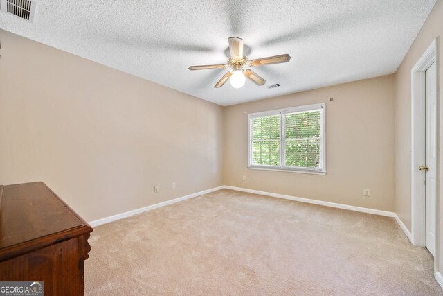 spare room featuring ceiling fan, light carpet, and a textured ceiling