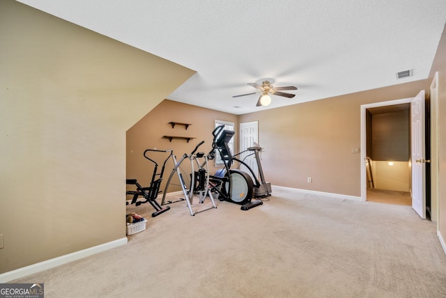 exercise area with ceiling fan, light colored carpet, and a textured ceiling