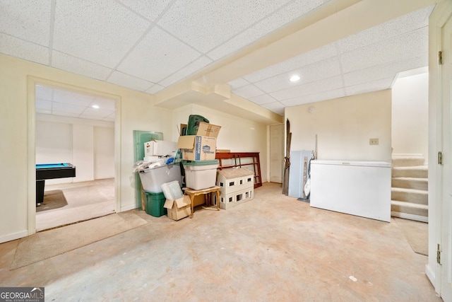 basement featuring pool table, a paneled ceiling, and refrigerator