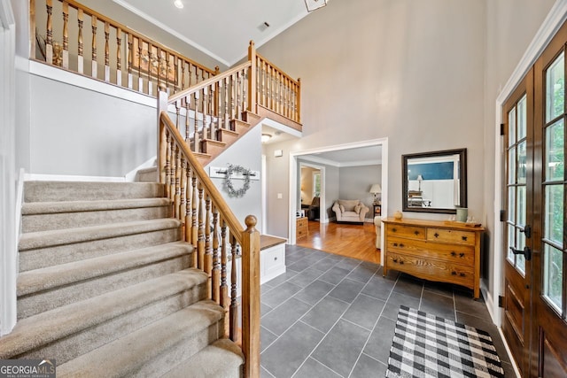 stairs with a towering ceiling, ornamental molding, french doors, and tile patterned floors