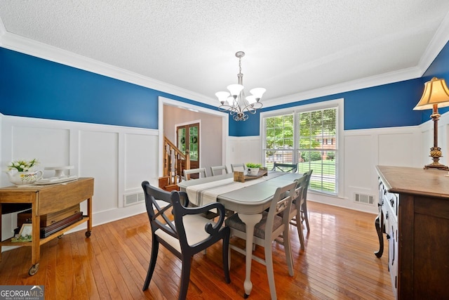 dining area featuring crown molding, light hardwood / wood-style floors, a chandelier, and a textured ceiling