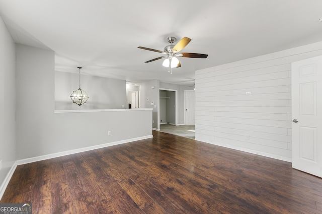 empty room with ceiling fan with notable chandelier, dark hardwood / wood-style flooring, and wood walls