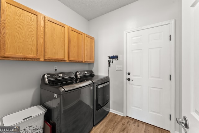 laundry area with a textured ceiling, light hardwood / wood-style floors, cabinets, and washing machine and clothes dryer