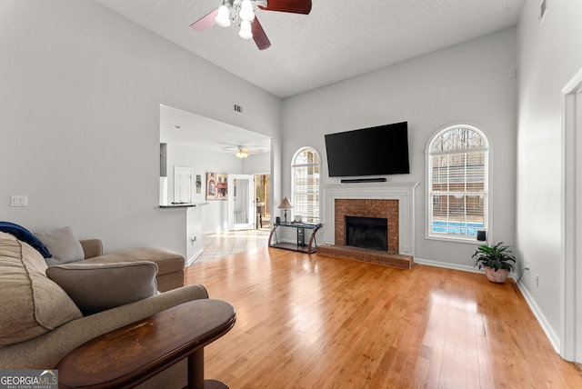 living room featuring a fireplace, a high ceiling, ceiling fan, a textured ceiling, and light hardwood / wood-style flooring