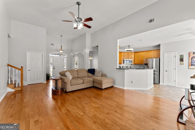 living room with ceiling fan, a towering ceiling, and light wood-type flooring