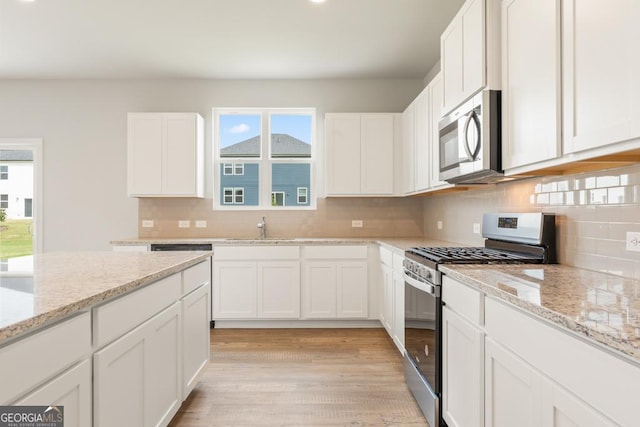 kitchen with tasteful backsplash, sink, white cabinets, stainless steel appliances, and light stone countertops