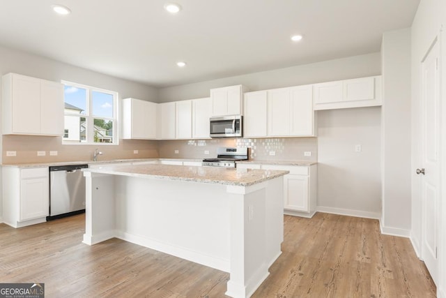 kitchen featuring light stone counters, appliances with stainless steel finishes, a kitchen island, white cabinets, and backsplash