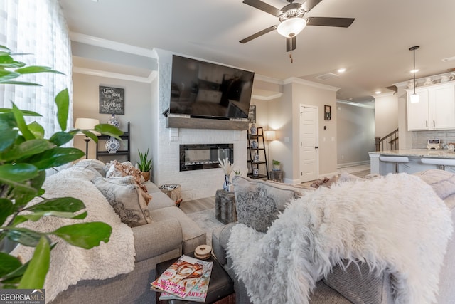 living room featuring crown molding, a large fireplace, ceiling fan, and light wood-type flooring