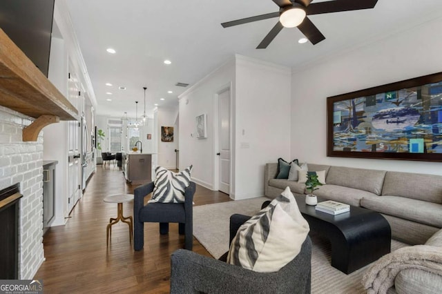 living room featuring crown molding, a brick fireplace, dark wood-type flooring, and ceiling fan