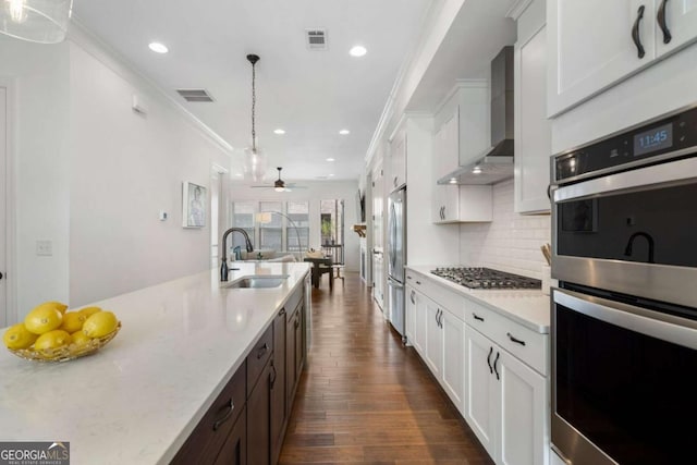 kitchen with pendant lighting, sink, wall chimney range hood, white cabinetry, and stainless steel appliances