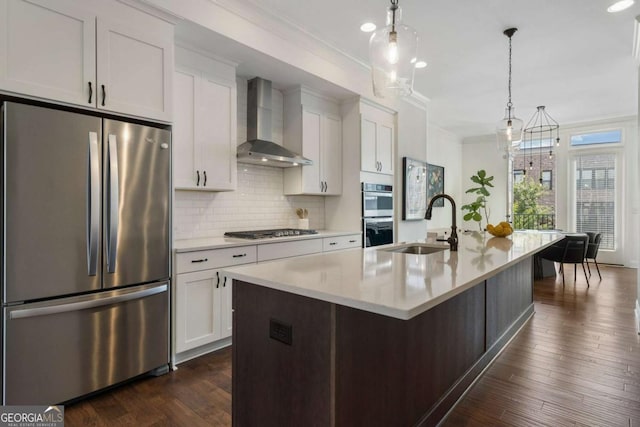 kitchen featuring appliances with stainless steel finishes, decorative light fixtures, a center island with sink, and wall chimney exhaust hood