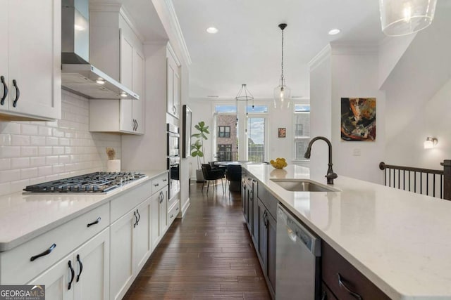 kitchen with wall chimney range hood, sink, a kitchen island with sink, hanging light fixtures, and stainless steel appliances