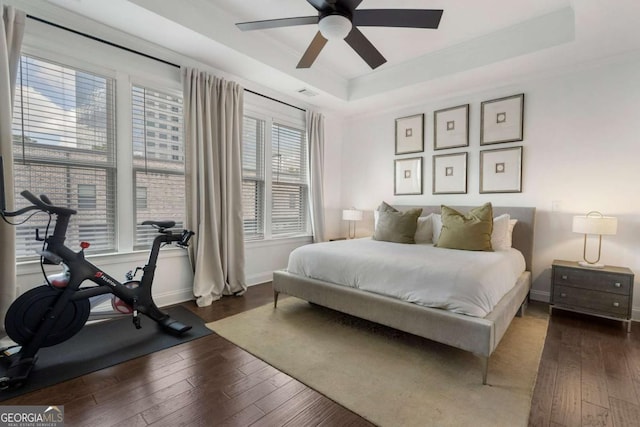 bedroom with dark hardwood / wood-style floors, ceiling fan, and a tray ceiling