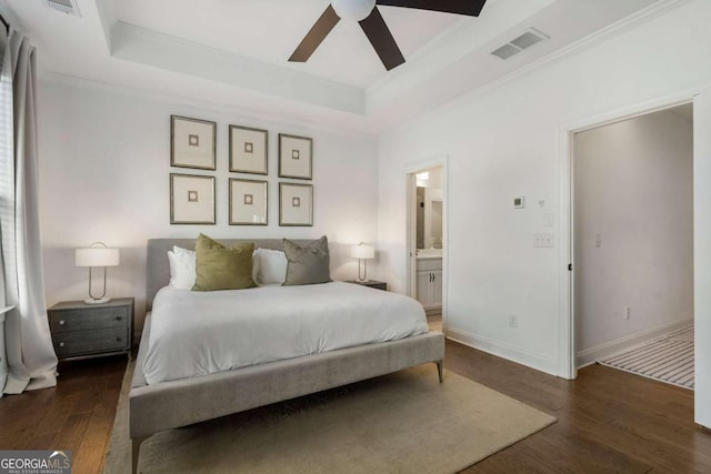 bedroom featuring dark hardwood / wood-style flooring, crown molding, ensuite bath, and a raised ceiling