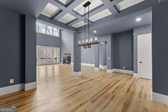 unfurnished living room with light wood finished floors, baseboards, coffered ceiling, and a glass covered fireplace