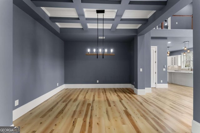 unfurnished dining area featuring baseboards, light wood-type flooring, coffered ceiling, and a notable chandelier