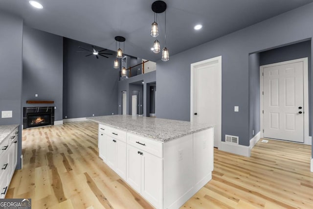 kitchen with light stone countertops, a kitchen island, white cabinets, and open floor plan