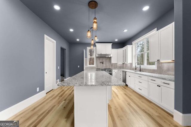 kitchen featuring a center island, decorative light fixtures, white cabinets, light stone countertops, and under cabinet range hood