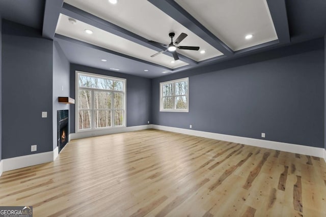 unfurnished living room with baseboards, ceiling fan, light wood-style flooring, beamed ceiling, and a lit fireplace