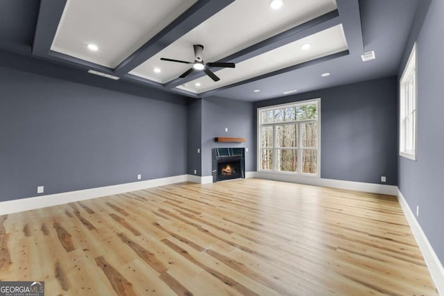 unfurnished living room with beam ceiling, light wood-type flooring, a warm lit fireplace, and baseboards