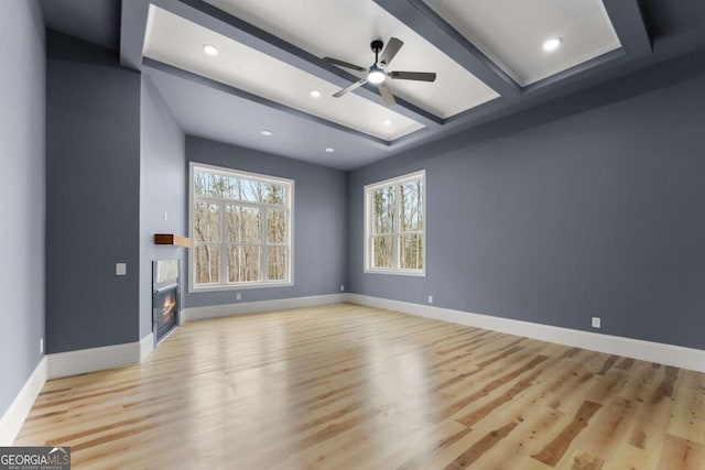 unfurnished living room featuring light wood finished floors, a glass covered fireplace, beam ceiling, and baseboards