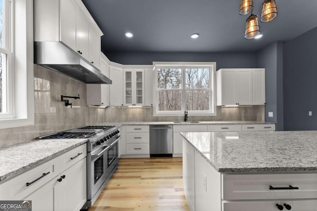 kitchen featuring decorative light fixtures, appliances with stainless steel finishes, glass insert cabinets, white cabinetry, and a sink