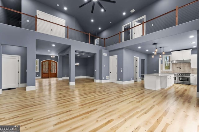 unfurnished living room featuring light wood-style flooring, baseboards, a ceiling fan, and french doors