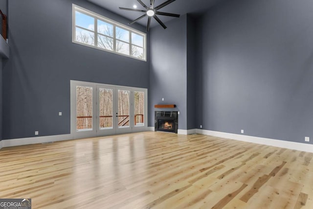 unfurnished living room with a warm lit fireplace, light wood finished floors, and baseboards