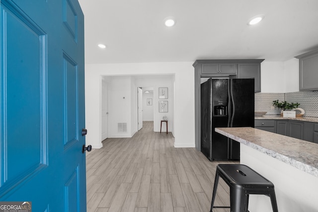 kitchen with gray cabinetry, backsplash, a kitchen breakfast bar, light hardwood / wood-style floors, and black refrigerator with ice dispenser