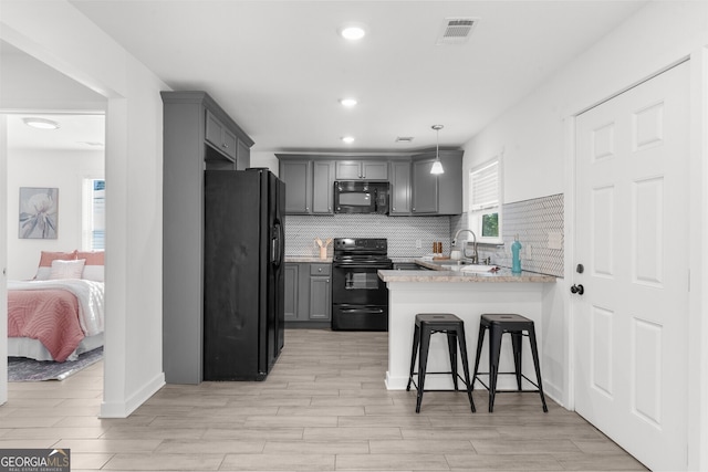 kitchen with a breakfast bar, gray cabinetry, black appliances, decorative light fixtures, and kitchen peninsula