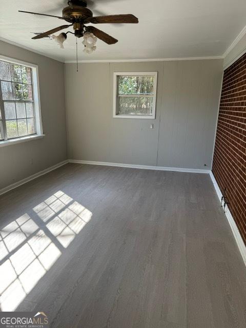 spare room featuring wood-type flooring, brick wall, ceiling fan, and crown molding