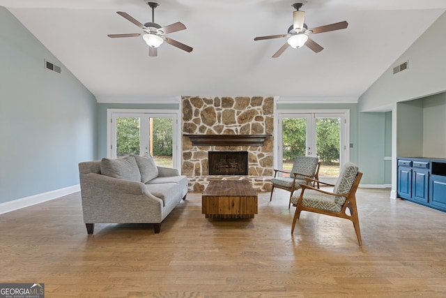 living room featuring french doors, ceiling fan, a stone fireplace, and light hardwood / wood-style floors