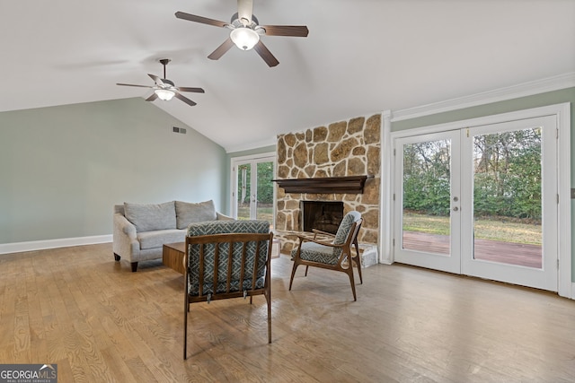 living room featuring vaulted ceiling, a stone fireplace, ceiling fan, light wood-type flooring, and french doors