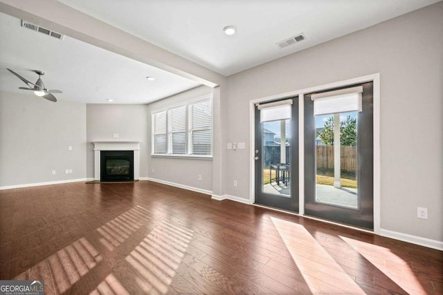 unfurnished living room with a wealth of natural light, wood-type flooring, a fireplace with flush hearth, and visible vents