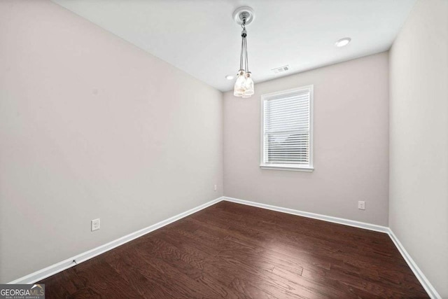 spare room with dark wood-type flooring, visible vents, and baseboards