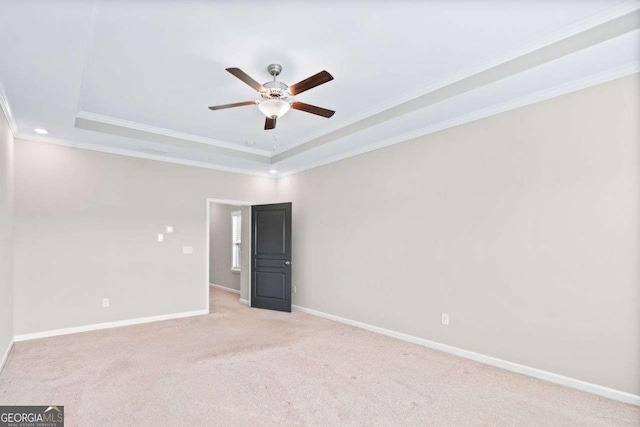 spare room featuring a raised ceiling, light carpet, crown molding, and baseboards