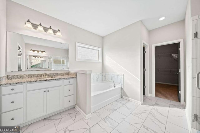 bathroom featuring marble finish floor, baseboards, a walk in closet, and a bath