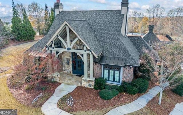 english style home featuring metal roof, roof with shingles, a standing seam roof, french doors, and brick siding