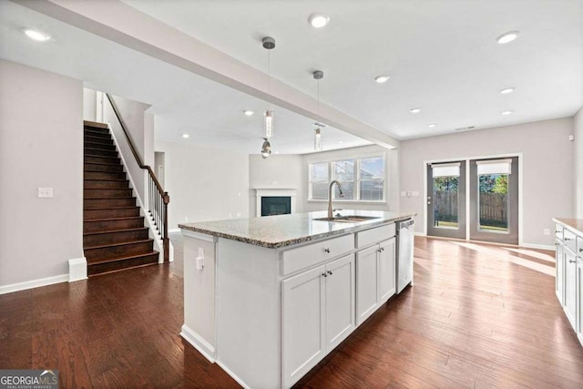 kitchen with stainless steel dishwasher, light stone counters, dark wood finished floors, and a sink