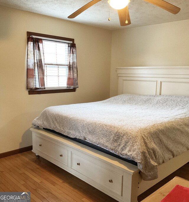 bedroom with ceiling fan, light hardwood / wood-style flooring, and a textured ceiling