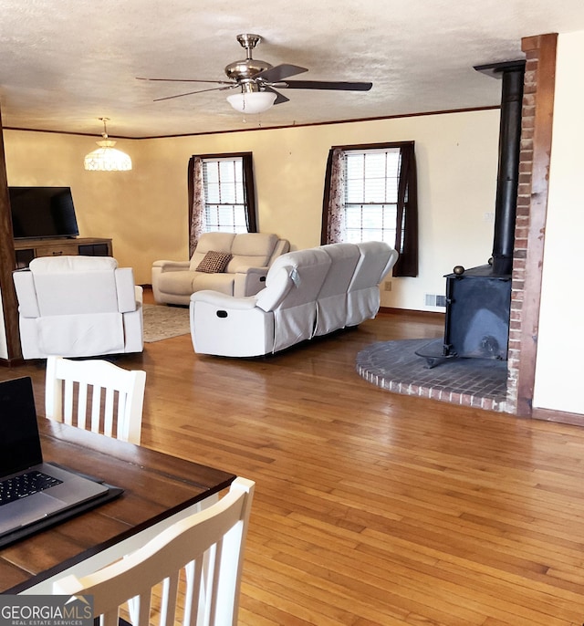 living room featuring ceiling fan, a wood stove, hardwood / wood-style floors, and a textured ceiling